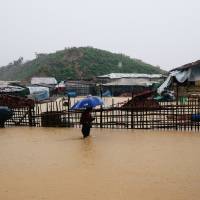 A Rohingya refugee walks along the water as parts of the Kutupalong camp flooded during heavy rain in Cox\'s Bazar, Bangladesh, Wednesday. | REUTERS