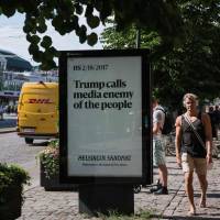 People walk next to an advertising board reading \"Trump calls media enemy of the people\" on the sidelines of a meeting between U.S. President and his Russian counterpart on Monday in Helsinki. | AFP-JIJI