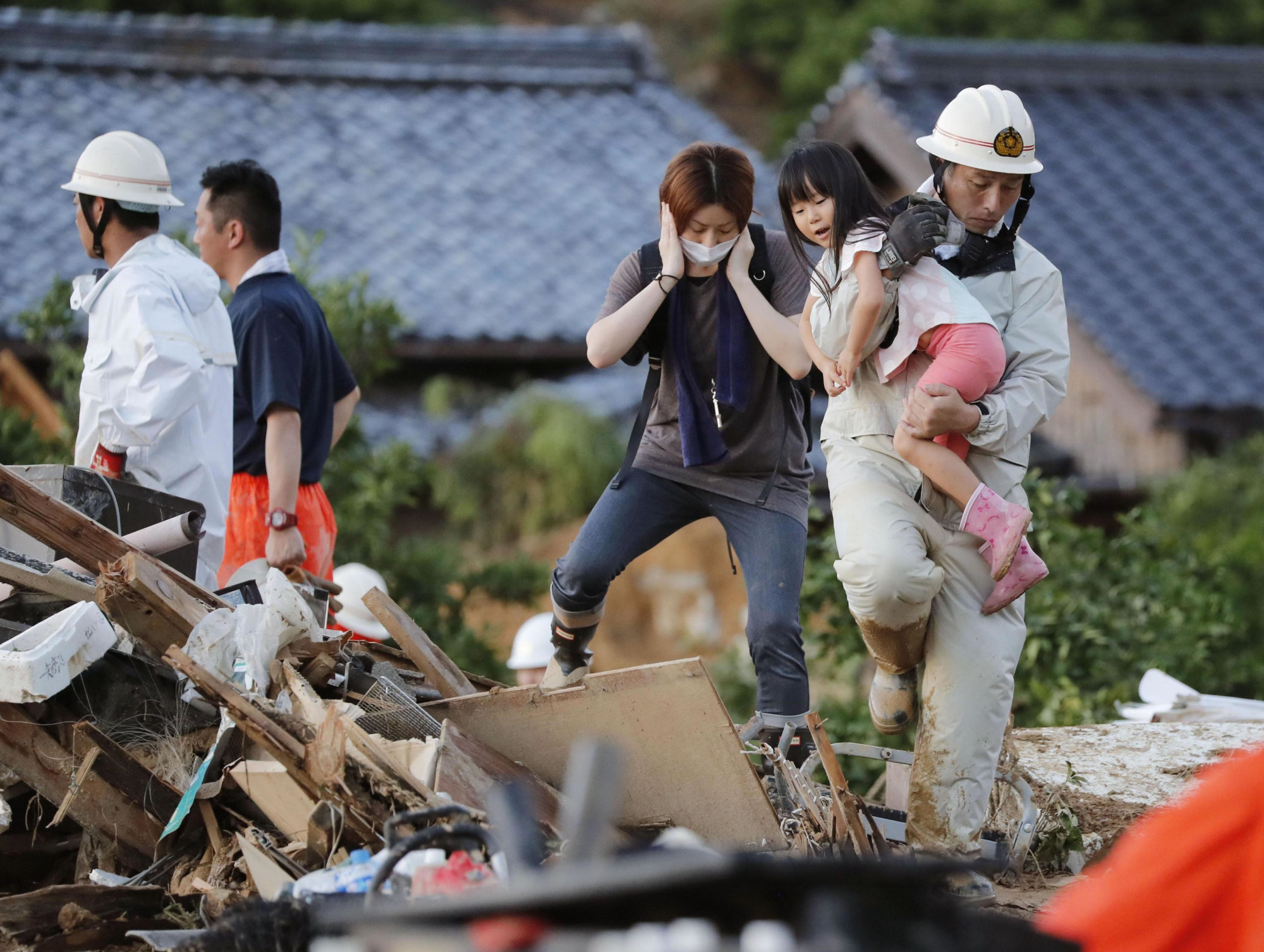 A firefighter carries a girl over debris Sunday evening in Uwajima, Ehime Prefecture. | KYODO