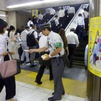 A East Japan Railway Co. employee at Tokyo Station hands out information Monday about its escalator safety campaign. | KYODO