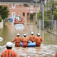 Rescuers help local residents evacuate in the flooded town of Saka, Hiroshima Prefecture, on Saturday. | KYODO