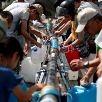 Local residents collect water supplies near a flooded area at Mihara Daini junior high school, which is acting as an emergency water station, in Mihara, Hiroshima Prefecture, on Monday. | REUTERS