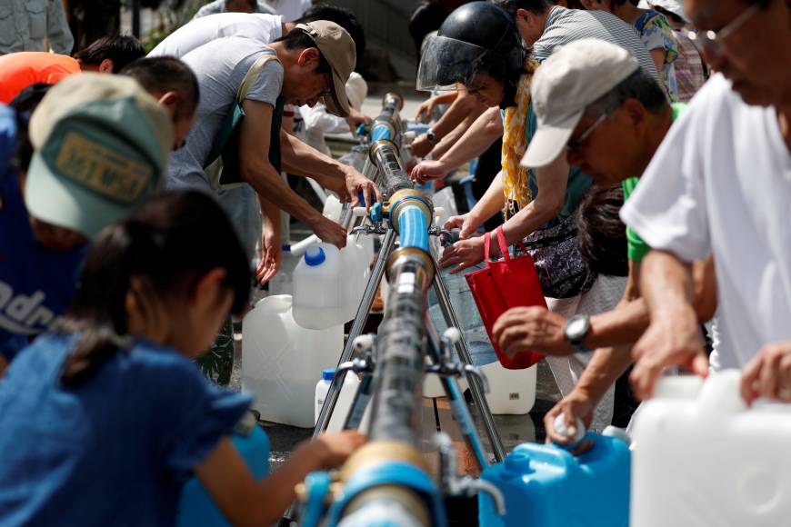 Local residents collect water supplies near a flooded area at Mihara Daini junior high school, which is acting as an emergency water station, in Mihara, Hiroshima Prefecture, on Monday.