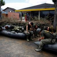 Rescue workers rest in an area of Kurashiki, Okayama Prefecture, on Sunday after heavy rains inundated western Japan. | REUTERS