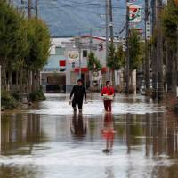 Men make their way in a flooded area of Kurashiki, Okayama Prefecture, on Sunday. | REUTERS