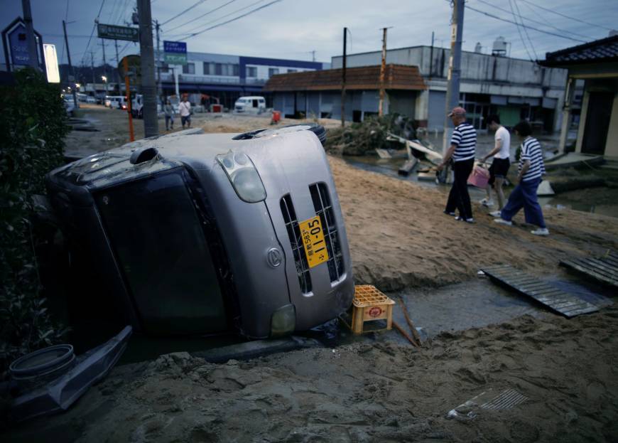 Local residents walk next to a damaged car in a flooded area of Kurashiki, Okayama Prefecture, on Sunday.