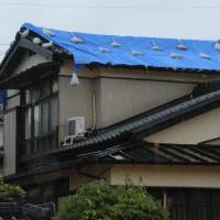 As heavy rain falls in Takatsuki, Osaka Prefecture, on Thursday, a house roof is seen covered with a blue plastic sheet. | KYODO
