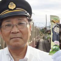 Choshi Electric Railway President Katsunori Takemoto shows off a snack called the Mazui Bo, or \"foul-tasting stick,\" in an effort to shore up the struggling railway\'s bottom line. | CHOSHI ELECTRIC RAILWAY / VIA KYODO