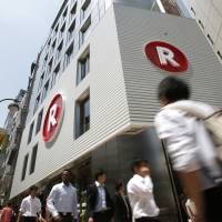 Pedestrians walk past a cafe operated by Rakuten Inc. in Tokyo. The e-commerce giant has an ambitious plan to build a cutting-edge wireless network to take on existing phone operators. | BLOOMBERG