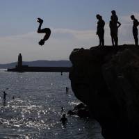 Young men leap off rocks into the ocean at Nice, south-eastern France, on Thursday as heatwave conditions prevail over Europe. | AFP-JIJI