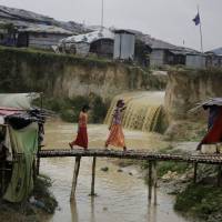 Rohingya refugee girls cross a makeshift bamboo bridge at the Kutupalong refugee camp, where they have been living amid uncertainty over their future after they fled Myanmar to escape violence a year ago, in Bangladesh Tuesday. | ALTAF QADRI / VIA AP