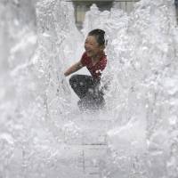 A boy enjoys himself as he cools off in an outdoor water fountain in Seoul on July 24. | AP