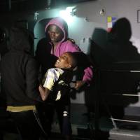 Migrants carry one of them off a boat as they arrive at a naval base in Tripoli, after being rescued off the coast of Zawia, about 45 km west of the Libyan capital Tripoli on Monday. Some 290 illegal immigrants from different African nationalities were rescued. | AFP-JIJI