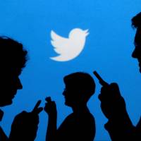 People holding mobile phones are silhouetted against a backdrop projected with the Twitter logo in this illustration photo. | REUTERS