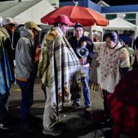 Venezuelan migrants waiting outside the Ecuadorean migration office at the Rumichaca international bridge in Tulcan, Ecuador, before crossing to Ipiales in Colombia, receive food from a group of Colombians who cross the border to help them, on Monday8. &#8212; Bogota said on Friday it was \"worried\" that tightened Ecuadorean entry requirements for Venezuelans fleeing an economic and political crisis would leave thousands stranded in Colombia. | LUIS ROBAYO / VIA AFP-JIJI
