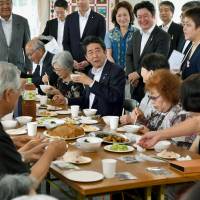 Prime Minister Shinzo Abe shares meals with evacuees from the March 11, 2011 disasters who are living at temporary housing in Ishinomaki, Miyagi Prefecture, on Thursday. | POOL / VIA KYODO