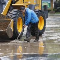 A man shovels upmud from a flooded parking lot in Mogami, Yamagata Prefecture, on Friday after the Mogamioguni River overflowed. | KYODO