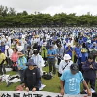 Protesters against a joint plan to relocate a U.S. military base in Okinawa observe a moment of silence Saturday for Gov. Takeshi Onaga, who died of cancer on Wednesday, at a park in Naha. | KYODO