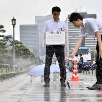 Tokyo Metropolitan Government officials on Monday conduct an experiment on a pedestrian walkway in Chiyoda Ward to test the effectiveness of spraying water to reduce surface temperatures. | KYODO