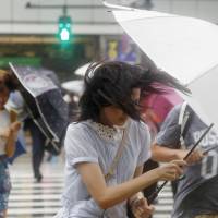 Pedestrians outside JR Shinjuku Station in Tokyo resist strong winds on Wednesday afternoon as Typhoon Shanshan approaches the eastern coast. | KYODO