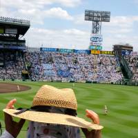 A fan adjusts a hat in the stands at Koshien Stadium. | LANCE HENDERSTEIN