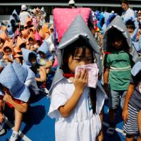 School children wearing padded hoods to protect them from falling debris take part in an earthquake simulation drill at an elementary school in Tokyo on Friday &#8212; a day before Disaster Prevention Day, which commemorates the 1923 Great Kanto earthquake. | REUTERS