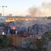 Smoke rises as people check the damage after a rocket hit a camp for displaced people during the fight between rival armed groups in Tripoli Sunday. | REUTERS