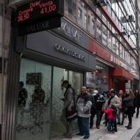 A sign displaying U.S. dollar exchange rates is displayed as people wait in line outside of a currency exchange shop in Buenos Aires on Aug. 30, as Argentina\'s currency crisis intensified while the peso plunged 20 percent. | BLOOMBERG