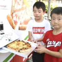 Children pull out freshly made pizza from a vending machine in Hiroshima on Sept. 2. | KYODO