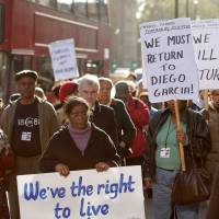 Chagos Islanders hold placards reading \"we must return to Diego Garcia\" and \"we\'ve right to live\" during a demonstration outside the London\'s Houses of Parliament, after British government won its appeal to Britain\'s highest court over previous rulings that allowed displaced Indian Ocean islanders to return home, in 2008. | SHAUN CURRY / VIA AFP-JIJI