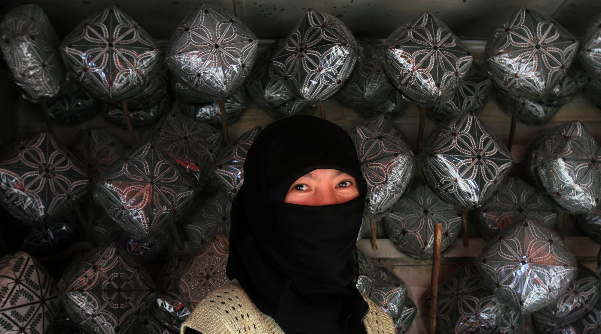 A vendor smiles behind her veil by Uighur hats on display for sale in Hetian, in China's Xinjiang province, in October 2006. | BLOOMBERG
