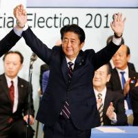 Prime Minister Shinzo Abe raises his hands alongside former Defense Minister Shigeru Ishiba at the Liberal Democratic Party\'s headquarters in Tokyo on Thursday after the prime minister won the party\'s leadership vote. | REUTERS