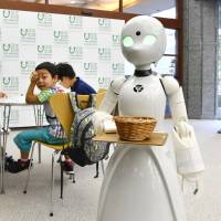 An OriHime-D robot, operated remotely by a severely disabled person at their home, serves customers at a cafe set up in Tokyo on a trial basis in August. | KYODO