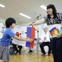 A Russian woman presents paintings made by Russian children at a nursery school in Mukawa, Hokkaido, on Saturday. | KYODO