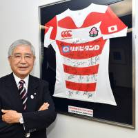 Akira Uehara poses before the autographed Japan rugby team\'s jersey earlier this month in his office at Taisho Pharmaceutical Co., Ltd. in Toshima Ward, Tokyo. | YOSHIAKI MIURA