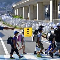 Students from Tenno Elementary School in Kure, Hiroshima Prefecture, return to school Monday for the new term after torrential rains in July triggered deadly mudslides and flooding in western Japan. Hundreds of sandbags used to fight the floods remain piled up on the roadside. | KYODO