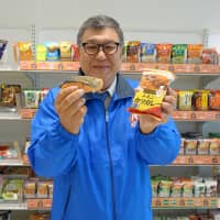 Masato Shimamura, technical adviser for Amano Foods, a brand owned by Asahi Group Foods, poses with a package of freeze-dried chicken cutlet curry and grilled salmon at the company\'s headquarters in Tokyo. | ALEX MARTIN