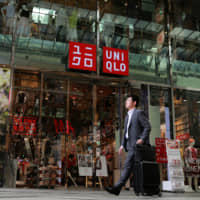 A pedestrian walks past Fast Retailing Co.\'s flagship Uniqlo store in Osaka in April. Strong sales supported the group\'s net profit, which rose to a record high in the year through August. | BLOOMBERG