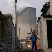 A man makes his through a village which is next to cooling towers of a coal-fired power plant in Shijiazhuang, in China\'s Hebei province, in 2015. | REUTERS