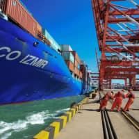 Workers pull a line from a cargo ship on Friday as it prepares to berth at a port in Qingdao, in China’s eastern Shandong province. | STR / VIA AFP-JIJI