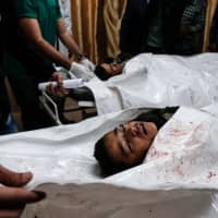 Palestinian doctors look at the bodies of Palestinians killed in an Israeli airstrike on the Gaza Strip, at the morgue of Al-Aqsa Hospital in Deir al-Balah in the central Gaza Strip on Sunday. &#8212; Three Palestinians were killed on Sunday in an Israeli airstrike on the Gaza Strip, the health ministry in the enclave said. | AFP-JIJI