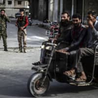 Fighters of the Syrian opposition stand near a checkpoint in northwestern city of Idlib, Syria, late Saturday. | UGUR CAN / DHA / VIA AP