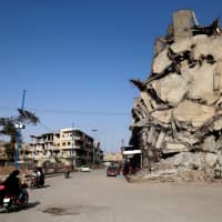 Syrians ride their motorcycles past a damaged building in the Syrian city of Raqqa on Thursday. A year after a U.S.-backed alliance of Syrian fighters drove the Islamic State group from the northern city of Raqa, traumatized civilians still live in fear of near-daily bombings. | AFP-JIJI