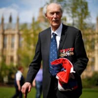 World War II Norwegian resistance fighter Joachim Roenneberg holds up a Union flag, which had been lowered from above the House of Lords, after it was presented to him by the Clerk of the House of Lords in Westminster, London, in 2013. | REUTERS