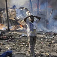 A man walks past a dead body and destroyed buildings at the scene of a blast in the capital Mogadishu on Oct. 14, 2017. Somalia is marking the first anniversary of one of the world\'s deadliest attacks since 9/11, a truck bombing in the heart of Mogadishu that killed well over 500 people. The Oct. 14, 2017 attack was so devastating that the al-Shabab extremist group that often targets the capital never claimed responsibility amid the local outrage. | AP
