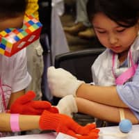 Girls experience life as a person with autism (left) or with a disability affecting the forearms and hands (right) through a game-like experience at the Lives Tokyo event in September at the Tokyo Midtown complex in Minato Ward. | MAGDALENA OSUMI