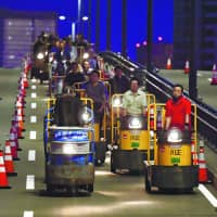 A convoy of electric carts and forklifts make the 2.3-kilometer-long journey from the closed Tsukiji fish market to the new Toyosu fish market in east Tokyo early on Sunday. Some 2,600 of the vehicles will eventually make the trip. The Toyosu market is scheduled to open Thursday. | KYODO