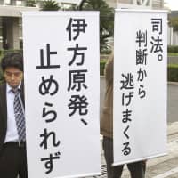 Signs saying \"Ikata nuclear power plant will not be suspended\" and \"Judicial power that is shy of handing down judgements\" are displayed in front of the Hiroshima District Court on Friday after the court rejected a call from residents to maintain the suspension of the plant. | KYODO