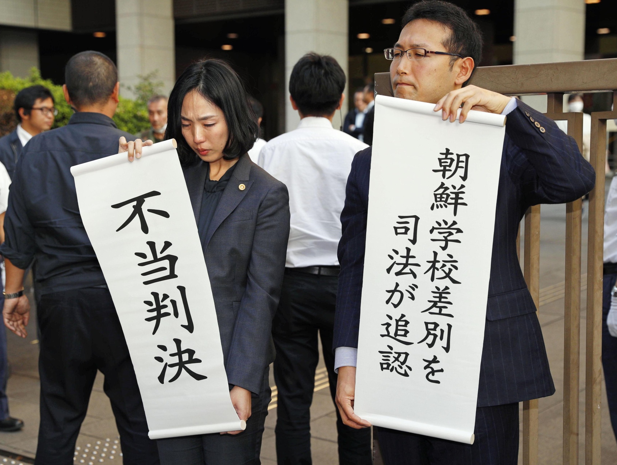 Supporters of former students from a pro-Pyongyang school involved in a lawsuit against the government over tuition waivers hold up protest signs on Tuesday in front of the Tokyo High Court. One of the signs calls a ruling denying the suit 'unreasonable.' | KYODO
