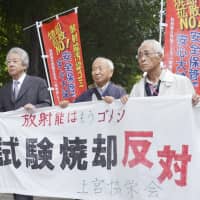 Plaintiffs hold a sign stating their opposition to the burning of radiation-tainted waste as they head to the Sendai District Court to file a lawsuit on Thursday. | KYODO